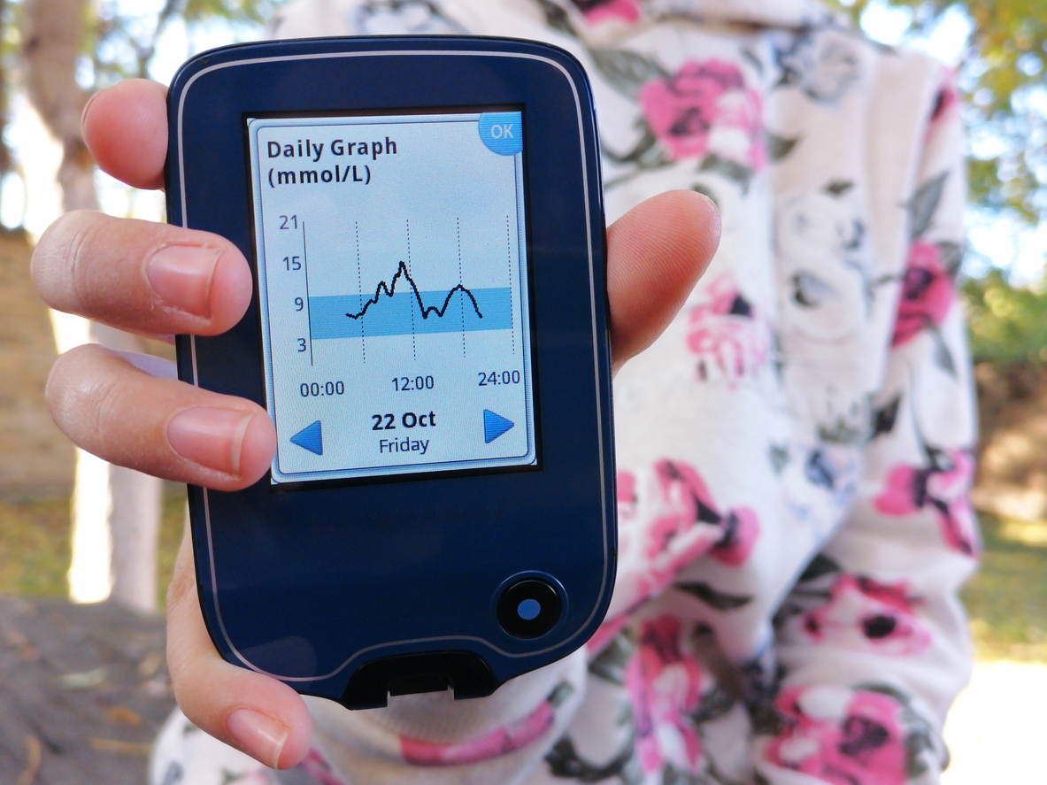 A woman holds up a FreeStyle Libre CGM 