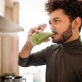 man drinking glass of green juice